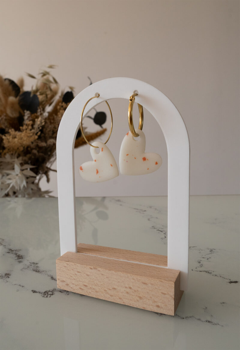 Apportez une touche d’élégance romantique à votre tenue grâce aux créoles avec cœur interchangeable, Aimée. Ces boucles d’oreilles artisanales se distinguent par un joli cœur asymétrique blanc et terracotta, posé sur une créole dorée ou argentée à choisir selon vos préférences. Polyvalentes, ultra légères et confortables, elles sublimeront aussi bien une tenue décontractée qu’un style plus sophistiqué.