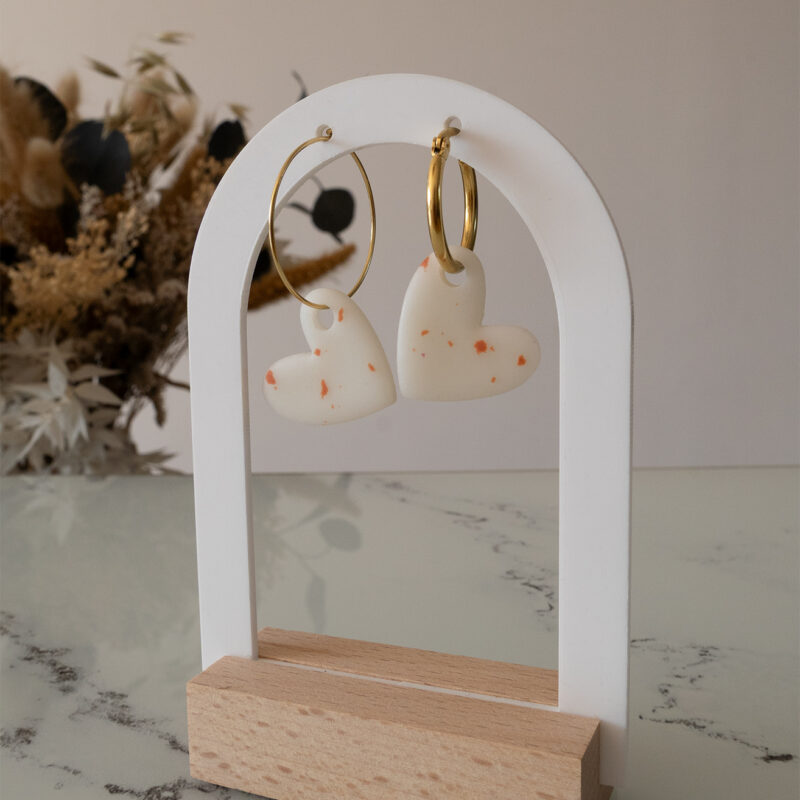 Apportez une touche d’élégance romantique à votre tenue grâce aux créoles avec cœur interchangeable, Aimée. Ces boucles d’oreilles artisanales se distinguent par un joli cœur asymétrique blanc et terracotta, posé sur une créole dorée ou argentée à choisir selon vos préférences. Polyvalentes, ultra légères et confortables, elles sublimeront aussi bien une tenue décontractée qu’un style plus sophistiqué.