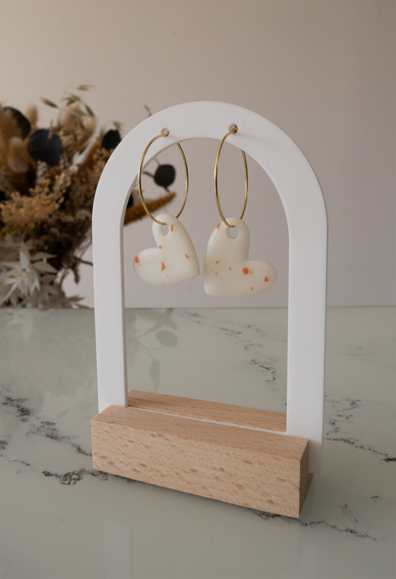 Apportez une touche d’élégance romantique à votre tenue grâce aux créoles avec cœur interchangeable, Aimée. Ces boucles d’oreilles artisanales se distinguent par un joli cœur asymétrique blanc et terracotta, posé sur une créole dorée ou argentée à choisir selon vos préférences. Polyvalentes, ultra légères et confortables, elles sublimeront aussi bien une tenue décontractée qu’un style plus sophistiqué.