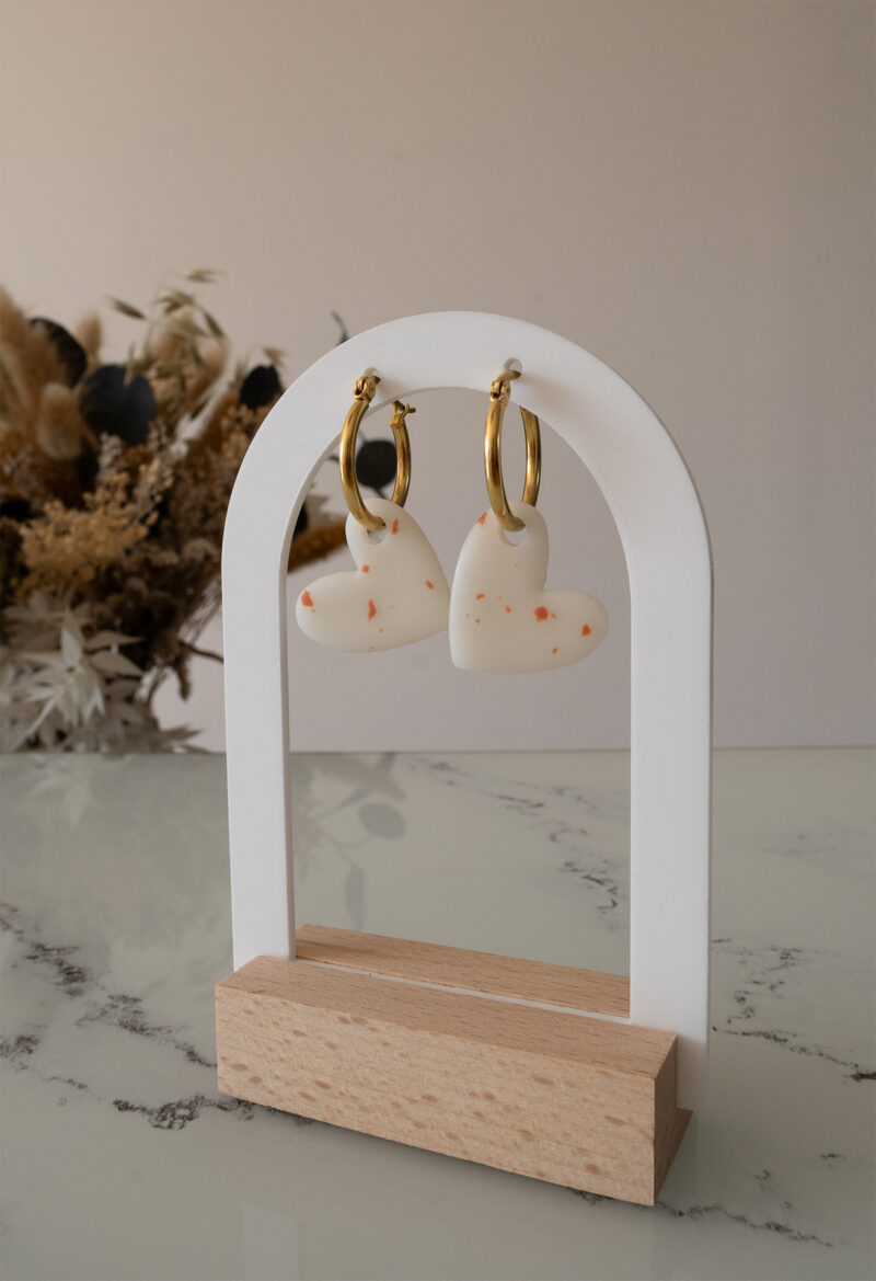 Apportez une touche d’élégance romantique à votre tenue grâce aux créoles avec cœur interchangeable, Aimée. Ces boucles d’oreilles artisanales se distinguent par un joli cœur asymétrique blanc et terracotta, posé sur une créole dorée ou argentée à choisir selon vos préférences. Polyvalentes, ultra légères et confortables, elles sublimeront aussi bien une tenue décontractée qu’un style plus sophistiqué.