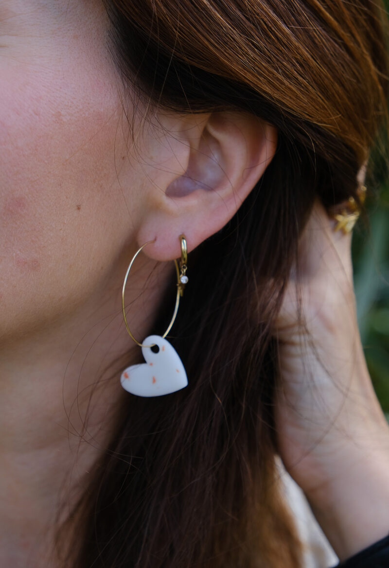 Apportez une touche d’élégance romantique à votre tenue grâce aux créoles avec cœur interchangeable, Aimée. Ces boucles d’oreilles artisanales se distinguent par un joli cœur asymétrique blanc et terracotta, posé sur une créole dorée ou argentée à choisir selon vos préférences. Polyvalentes, ultra légères et confortables, elles sublimeront aussi bien une tenue décontractée qu’un style plus sophistiqué.