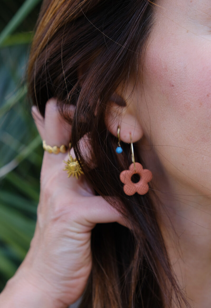 Apportez une touche poétique à vos looks avec les créoles avec fleurs interchangeables April. Ces boucles d’oreilles délicates se distinguent par une fine fleur à cinq pétales, de couleur terracotta et avec une joli texture, posée sur une créole à choisir selon vos préférences. Inspirées par la nature, polyvalentes et confortables, elles sublimeront aussi bien une tenue décontractée qu’un style plus sophistiqué. Elles sont réversibles,