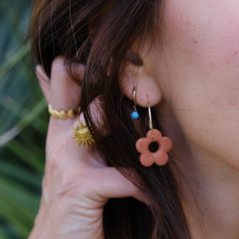 Apportez une touche poétique à vos looks avec les créoles avec fleurs interchangeables April. Ces boucles d’oreilles délicates se distinguent par une fine fleur à cinq pétales, de couleur terracotta et avec une joli texture, posée sur une créole à choisir selon vos préférences. Inspirées par la nature, polyvalentes et confortables, elles sublimeront aussi bien une tenue décontractée qu’un style plus sophistiqué. Elles sont réversibles,