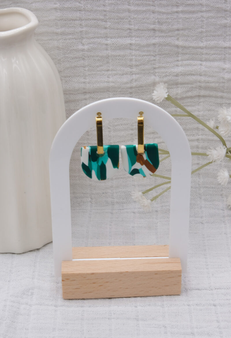 Apportez une touche de modernité à votre tenue grâce aux créoles avec pampille interchangeable, Inès. Ces boucles d’oreilles délicates se distinguent par un demi cercle marbré de différentes teintes de vert, de blanc et de doré. Il est posé sur une créole dorée ou argentée, à choisir selon vos préférences.
