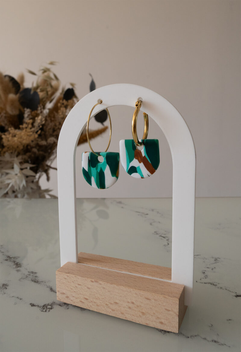 Apportez une touche de modernité à votre tenue grâce aux créoles avec pampille interchangeable, Inès. Ces boucles d’oreilles délicates se distinguent par un demi cercle marbré de différentes teintes de vert, de blanc et de doré. Il est posé sur une créole dorée ou argentée, à choisir selon vos préférences.