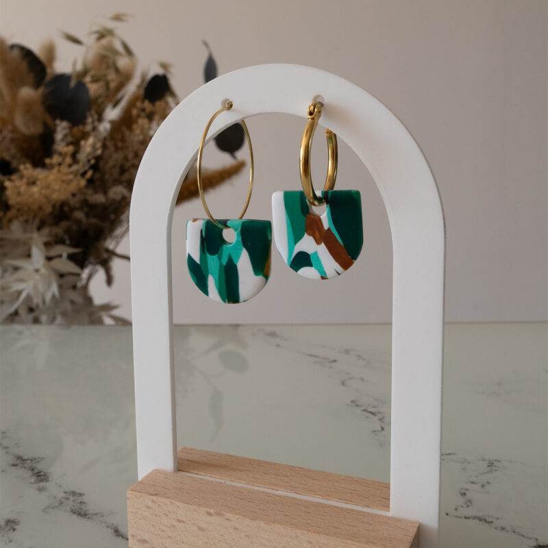Apportez une touche de modernité à votre tenue grâce aux créoles avec pampille interchangeable, Inès. Ces boucles d’oreilles délicates se distinguent par un demi cercle marbré de différentes teintes de vert, de blanc et de doré. Il est posé sur une créole dorée ou argentée, à choisir selon vos préférences.