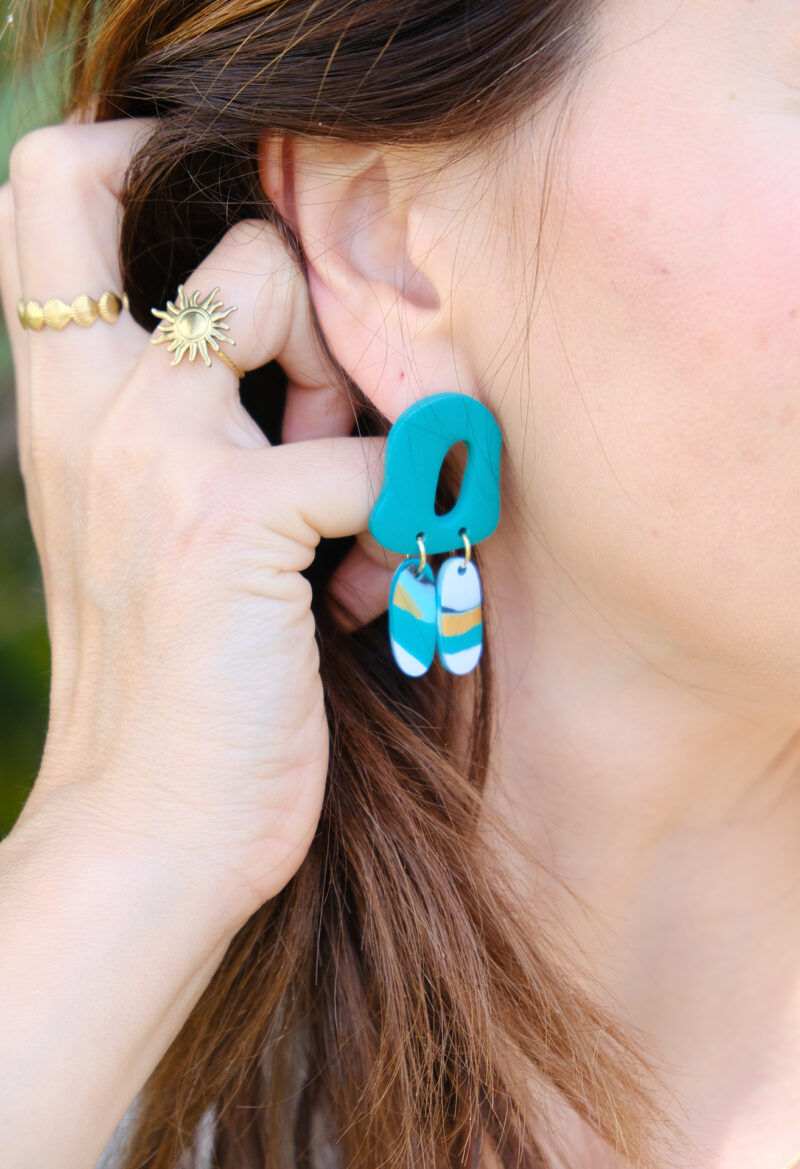 Découvrez le modèle Lisette, des boucles d’oreilles pendantes qui associent une pièce principale aux courbes abstraites à deux petits rectangles arrondis qui dansent subtilement à chaque mouvement, tels des plumes. Confectionnées à la main en argile polymère, légères et audacieuses, les Lisette insufflent une touche de créativité à vos looks.