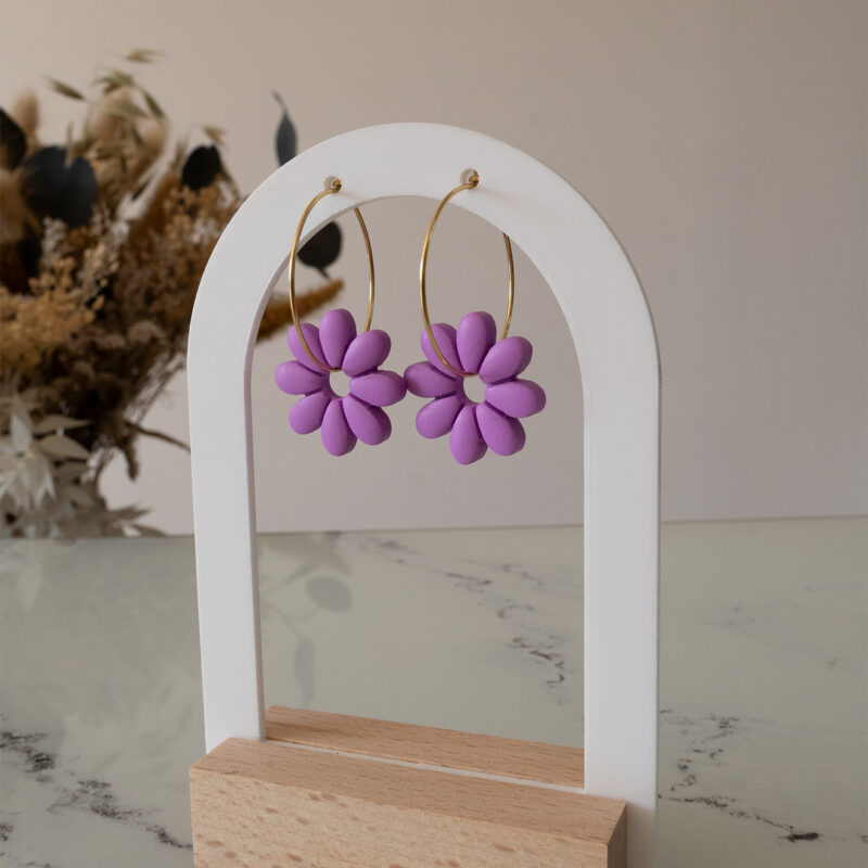 Apportez une touche de tendresse à votre tenue grâce aux créoles avec fleurs interchangeables, Marguerite. Ces boucles d’oreilles délicates se distinguent par une marguerite lilas posée sur une créole dorée ou argentée, à choisir selon vos préférences.