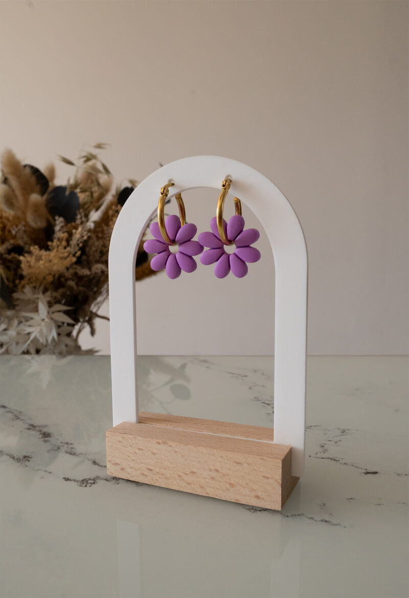 Apportez une touche de tendresse à votre tenue grâce aux créoles avec fleurs interchangeables, Marguerite. Ces boucles d’oreilles délicates se distinguent par une marguerite lilas posée sur une créole dorée ou argentée, à choisir selon vos préférences.
