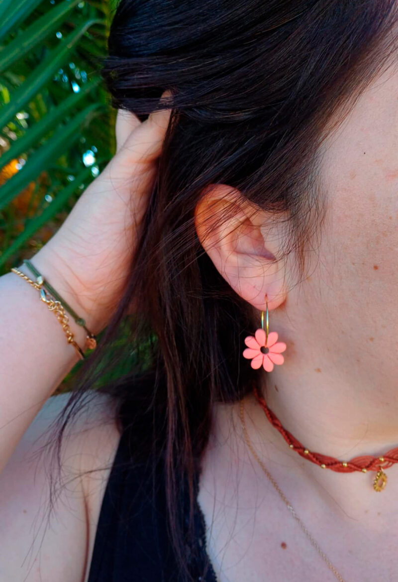 Apportez une touche de tendresse à votre tenue grâce aux créoles avec fleurs interchangeables, Marguerite. Ces boucles d’oreilles délicates se distinguent par une marguerite couleur pamplemousse, posée sur une créole dorée ou argentée, à choisir selon vos préférences.