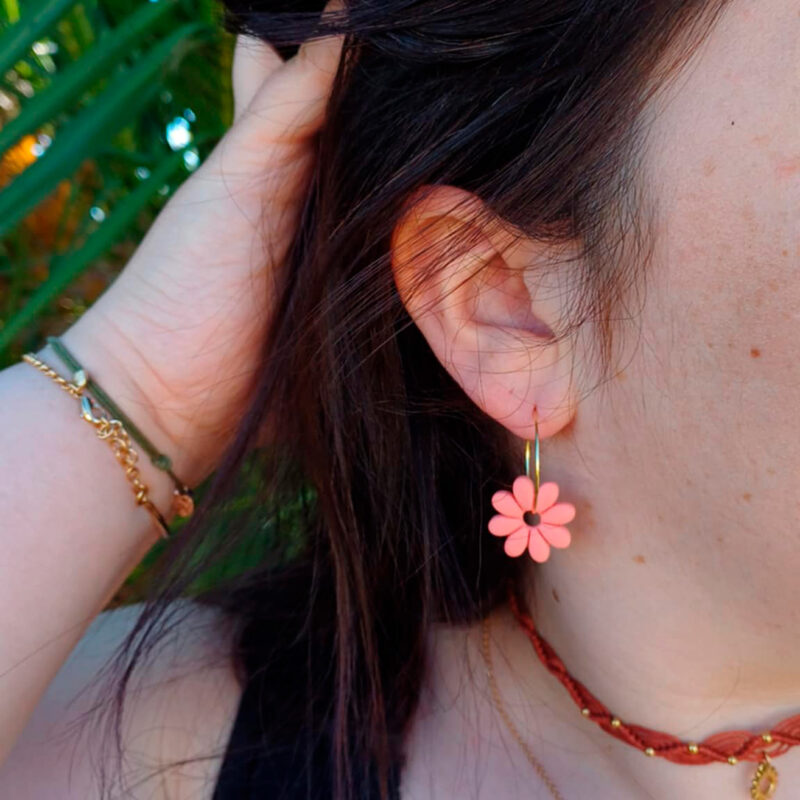 Apportez une touche de tendresse à votre tenue grâce aux créoles avec fleurs interchangeables, Marguerite. Ces boucles d’oreilles délicates se distinguent par une marguerite couleur pamplemousse, posée sur une créole dorée ou argentée, à choisir selon vos préférences.
