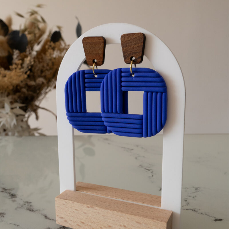 Découvrez Tara, des boucles d’oreilles pendantes qui associent une pièce rectangulaire en bois à un carré aux bord arrondi façonné à la main, en argile polymère bleu roi.Ultra-légères et confortables, ces boucles faites main sont conçues pour révéler votre singularité et donner du caractère à votre tenue.