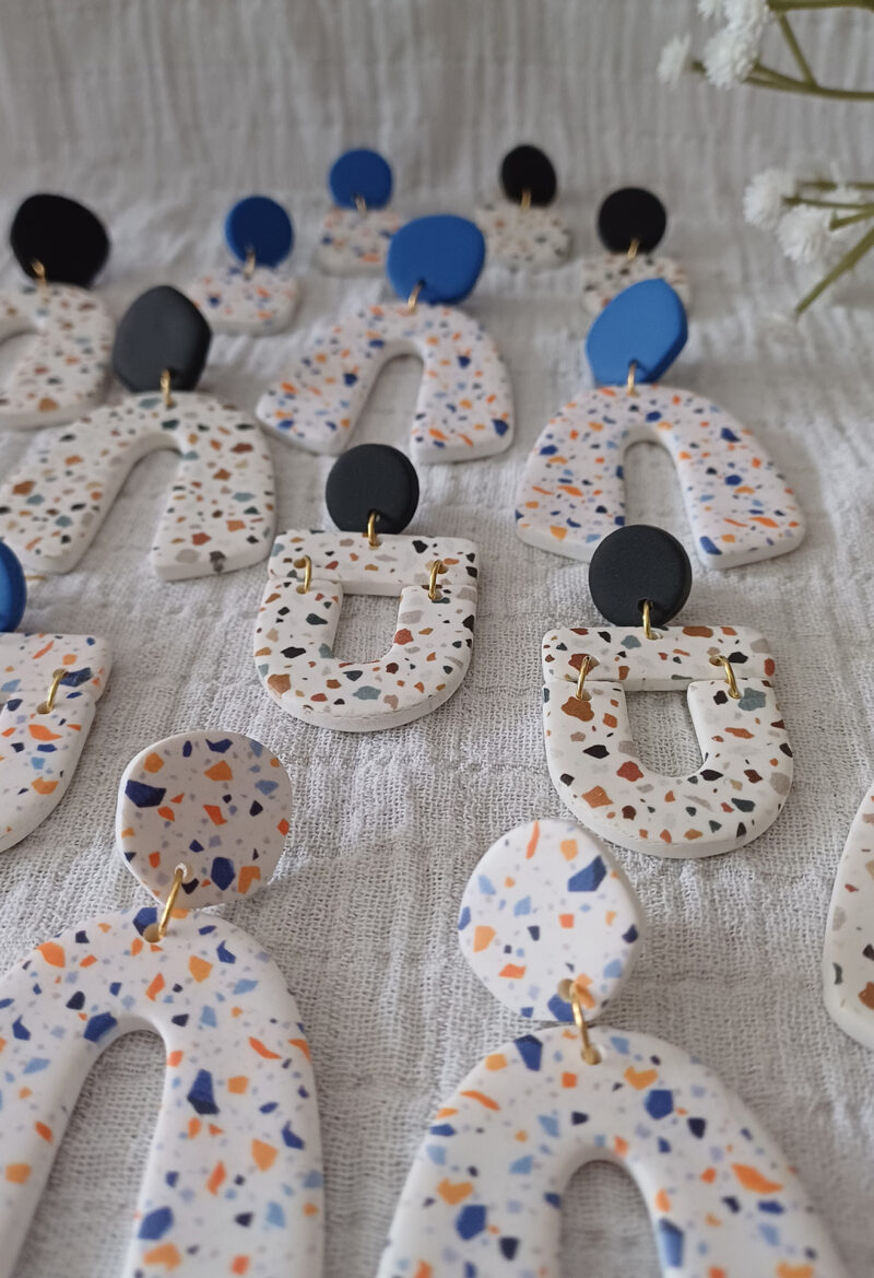 Des grosses boucles d'oreilles faites main avec arche, en terrazzo noir et marron ou bleu et orange. Des boucles d'oreilles pendantes, tendance à l'allure bohème. A s'offrir sur le site Un Bijou dans la Mare.