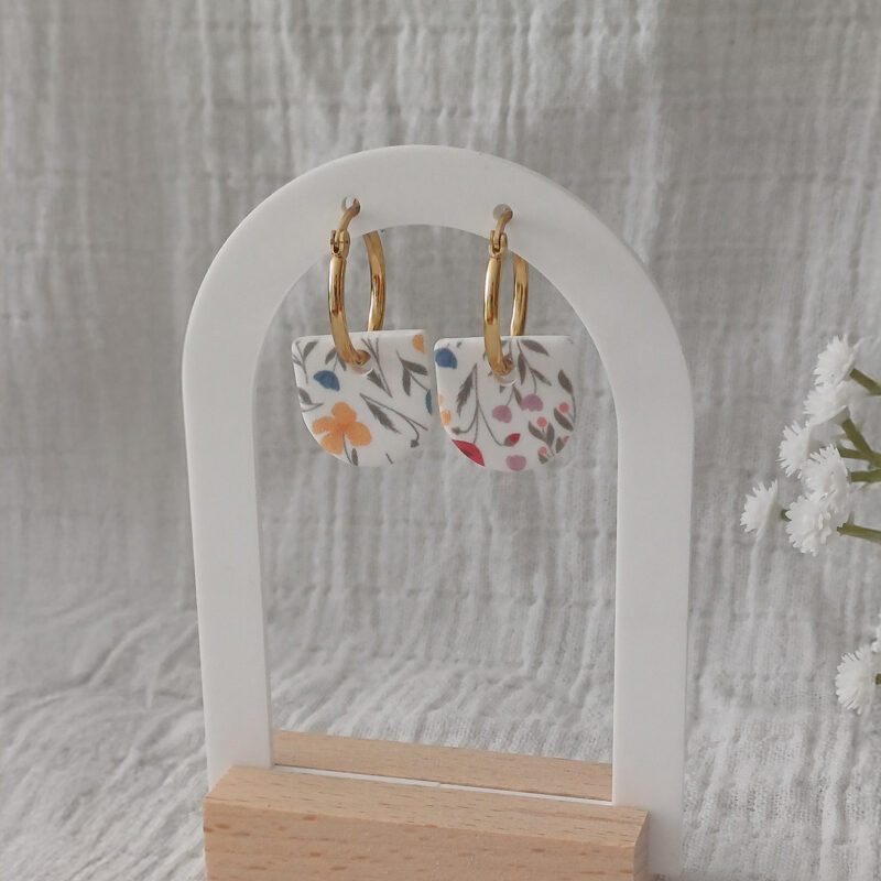 Apportez une touche de poésie à votre tenue grâce aux créoles avec pampille interchangeable, Inès. Ces boucles d’oreilles délicates se distinguent par un demi cercle avec un motif floral rare et breveté aux couleurs douces et apaisantes. Il est posé sur une créole dorée ou argentée, à choisir selon vos préférences. Polyvalentes, ultra légères et confortables, elles sublimeront aussi bien une tenue décontractée qu'un style plus sophistiqué. Les créoles sont en acier inoxydable (sans plomb, sans cadmium, sans nickel), les pampilles, elles, sont faites main en argile polymère.