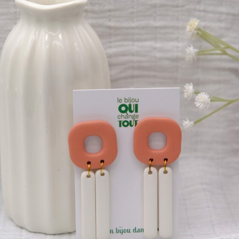 Découvrez le modèle Maggie, des boucles d'oreilles pendantes, faites main en argile polymère de couleur blanche et pêche, idéales pour l'été.