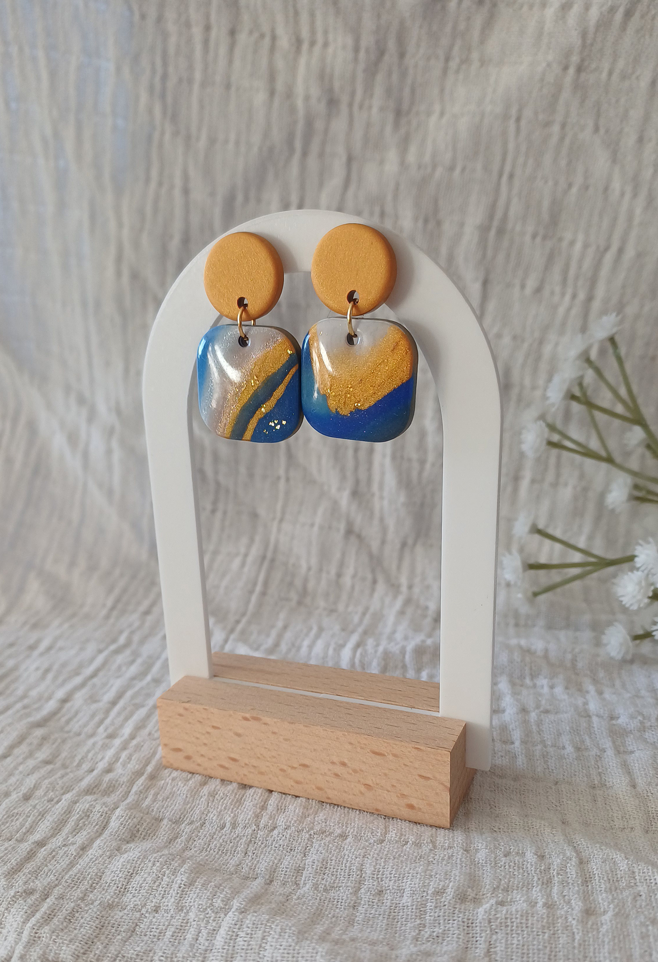 Ajoutez une touche de modernité minimaliste à votre style avec les boucles d’oreilles faites main Élodie. Ces pièces uniques associent un rond d’un beau doré nacré à un carré aux bords arrondis, marbré avec 3 couleurs de bleu différents, du blanc du noir et du doré nacré. Parfaites pour toutes les occasions, elles apportent une subtilité contemporaine à vos tenues, qu’elles soient casual ou habillées.