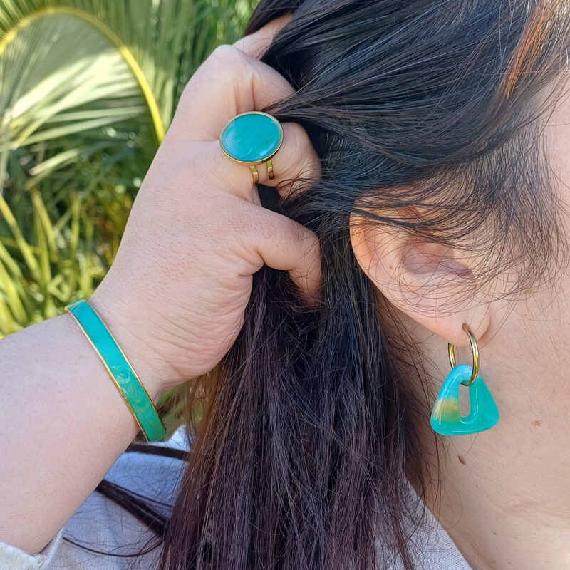 Le jonc Virginie en argile polymère et laiton doré allie finesse et caractère dans un design à la fois moderne et intemporel. Son cabochon en argile polymère transparente, façonné à la main, révèle des nuances inspirées de la pierre Amazonite avec son mélange subtil de vert, de blanc et de doré qui capte la lumière et change selon l’angle. Ce jonc s’adapte confortablement à tous les poignets. Retrouvez également la bague et les créoles intergangeables pour faire une parure.