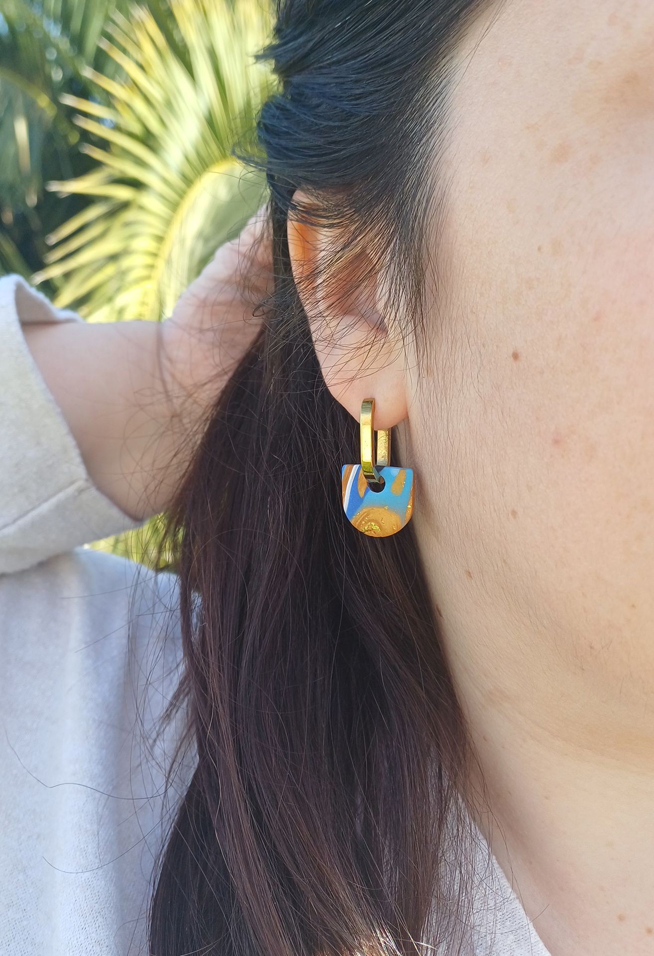 Apportez une touche de modernité à votre tenue grâce aux créoles avec pampille interchangeable, Inès. Ces boucles d’oreilles délicates se distinguent par un demi cercle marbré de différentes teintes de bleu, de blanc et de doré. Il est posé sur une créole dorée ou argentée, à choisir selon vos préférences.