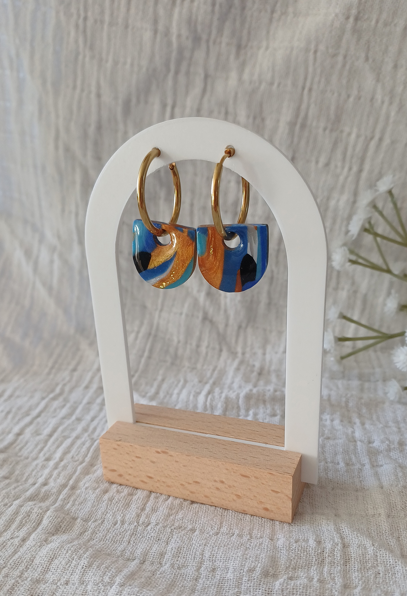 Apportez une touche de modernité à votre tenue grâce aux créoles avec pampille interchangeable, Inès. Ces boucles d’oreilles délicates se distinguent par un demi cercle marbré de différentes teintes de bleu, de blanc et de doré. Il est posé sur une créole dorée ou argentée, à choisir selon vos préférences.