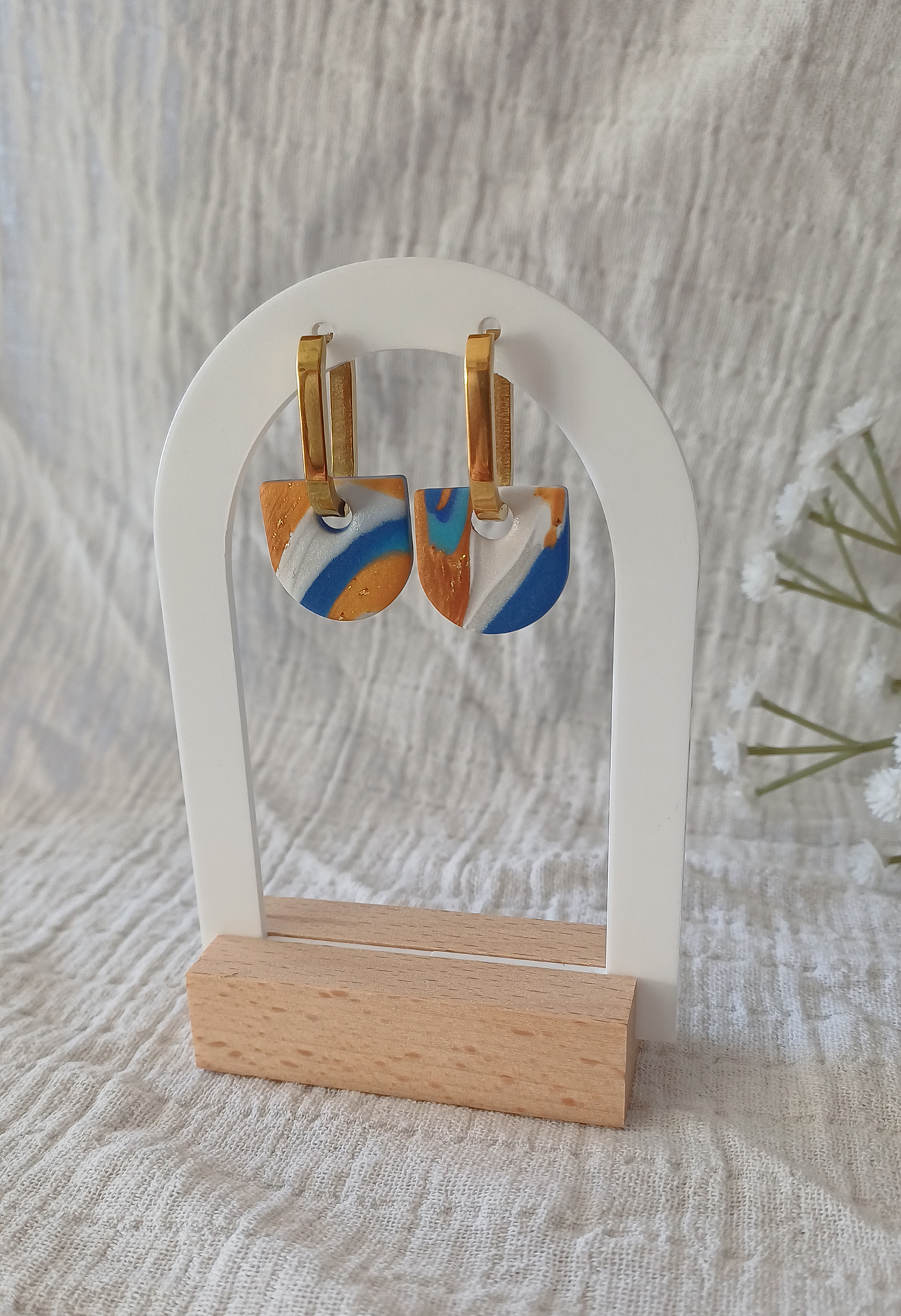 Apportez une touche de modernité à votre tenue grâce aux créoles avec pampille interchangeable, Inès. Ces boucles d’oreilles délicates se distinguent par un demi cercle marbré de différentes teintes de bleu, de blanc et de doré. Il est posé sur une créole dorée ou argentée, à choisir selon vos préférences.