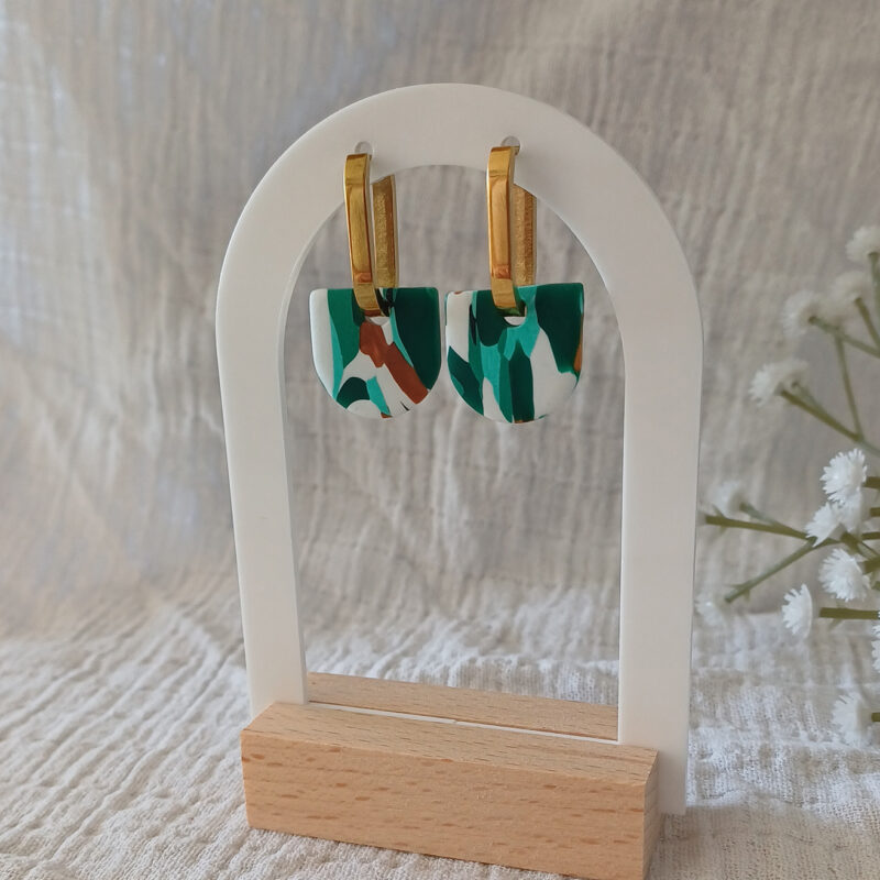 Apportez une touche de modernité à votre tenue grâce aux créoles avec pampille interchangeable, Inès. Ces boucles d’oreilles délicates se distinguent par un demi cercle marbré de différentes teintes de vert, de blanc et de doré. Il est posé sur une créole dorée ou argentée, à choisir selon vos préférences.