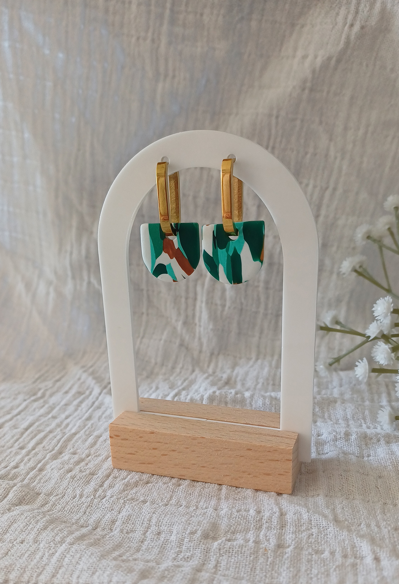 Apportez une touche de modernité à votre tenue grâce aux créoles avec pampille interchangeable, Inès. Ces boucles d’oreilles délicates se distinguent par un demi cercle marbré de différentes teintes de vert, de blanc et de doré. Il est posé sur une créole dorée ou argentée, à choisir selon vos préférences.